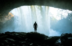 Figure in cave looking out through a waterfall